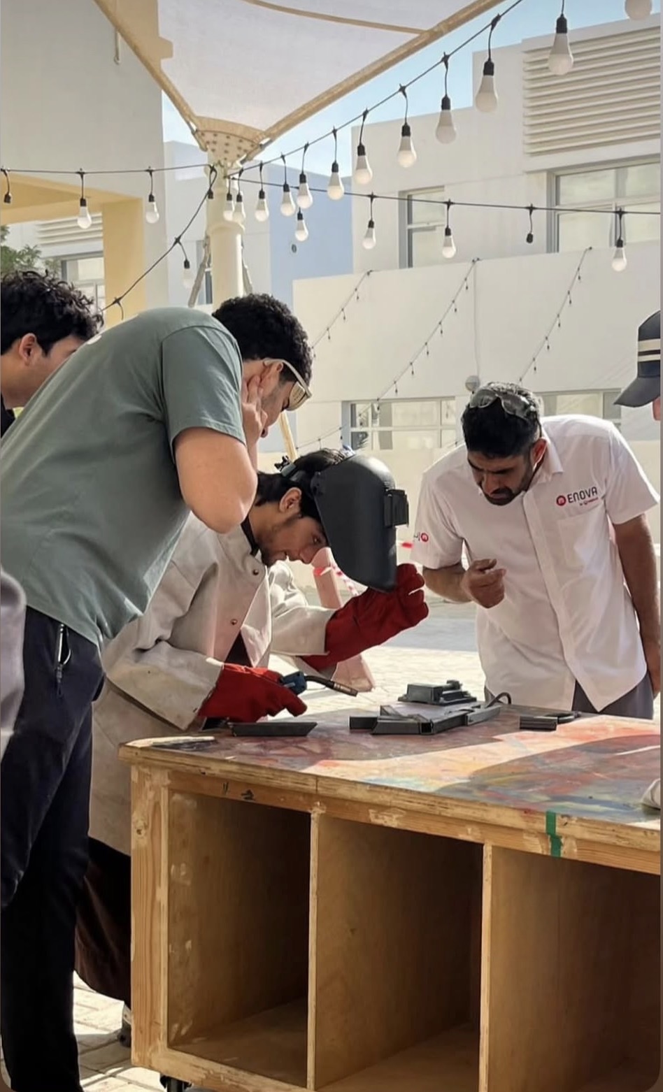An instructor leaning in over a weld while the team watches